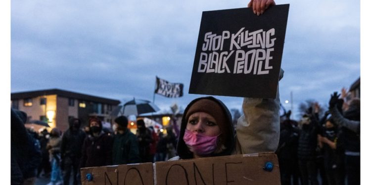A demonstrator holds a sign reading "Stop Killing Black People" as she stands outside the Brooklyn Center police station while protesting the death of Daunte Wright who was shot and killed by a police officer in Brooklyn Center, Minnesota on April 14, 2021.